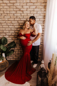 Mom and dad posing for maternity portraits in maternity studio in red dress. 
