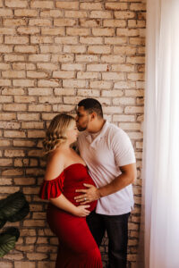 Dad kissing mom on forehead for maternity portraits in red dress for maternity studio picture session
