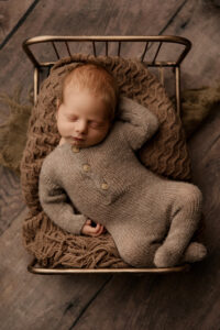 Newborn baby posing in knit romper on gold bed for portraits