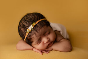 Baby posing on yellow backdrop for newborn session