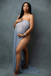 Black woman posing for pregnancy fine art photograph for maternity portraits in phoenix. Covered in blue chiffon