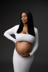 African American mother posing in white dress for maternity pictures in phoenix portrait studio