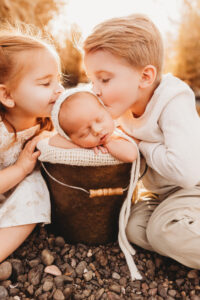 Two toddler siblings kissing their newborn baby brother in a newborn session at the river 