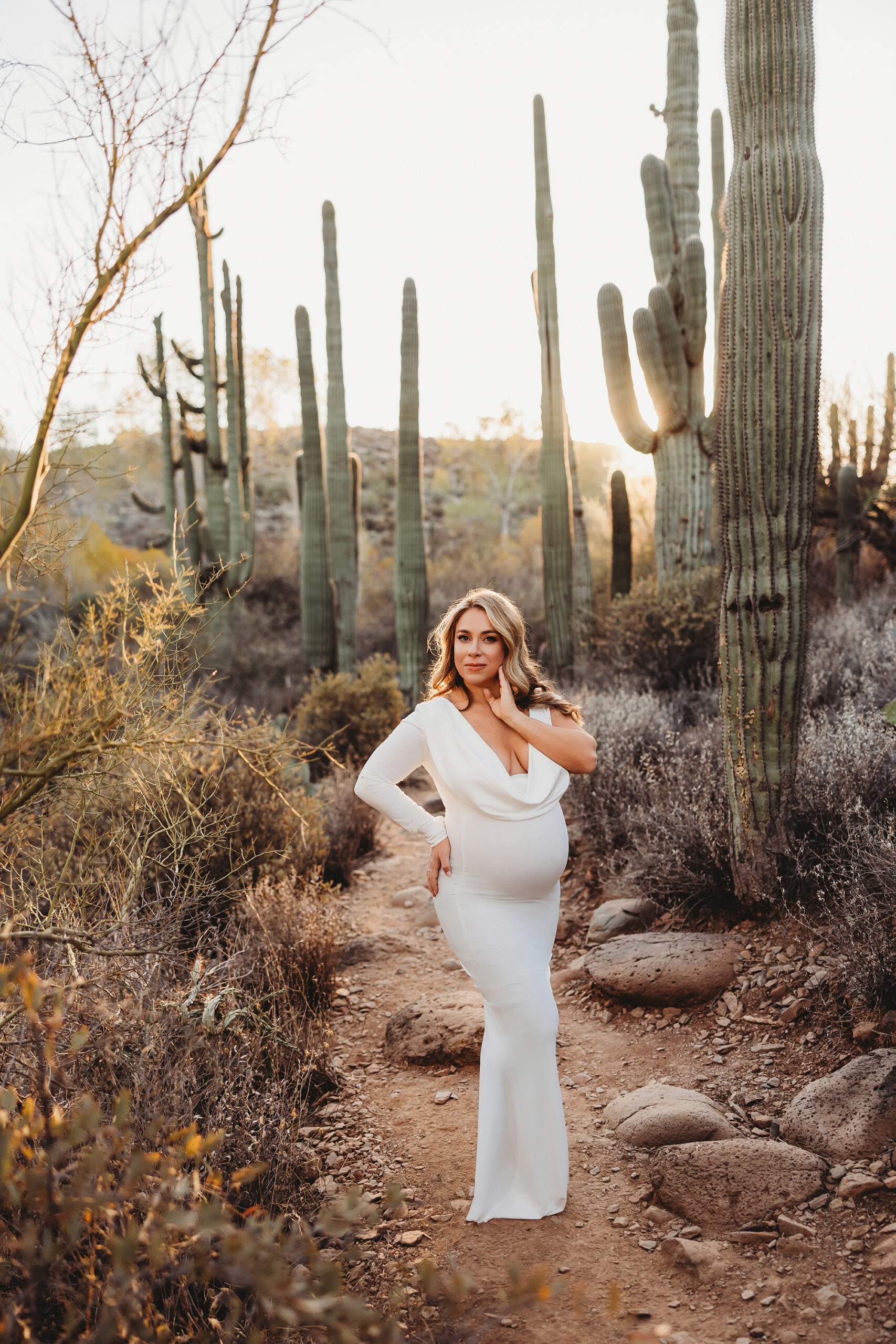 Pregnant mom posing for pregnancy pictures in white dress with large saguaro cacti