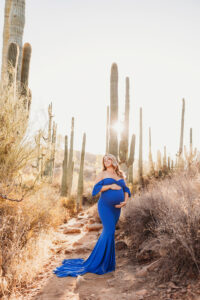 Mom posing for sunset maternity session with cacti in desert in blue dress