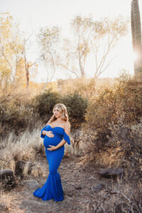 Mom posing for sunset maternity session with cacti in desert in blue dress