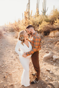 Mom and dad posing for sunset maternity session with cacti in desert