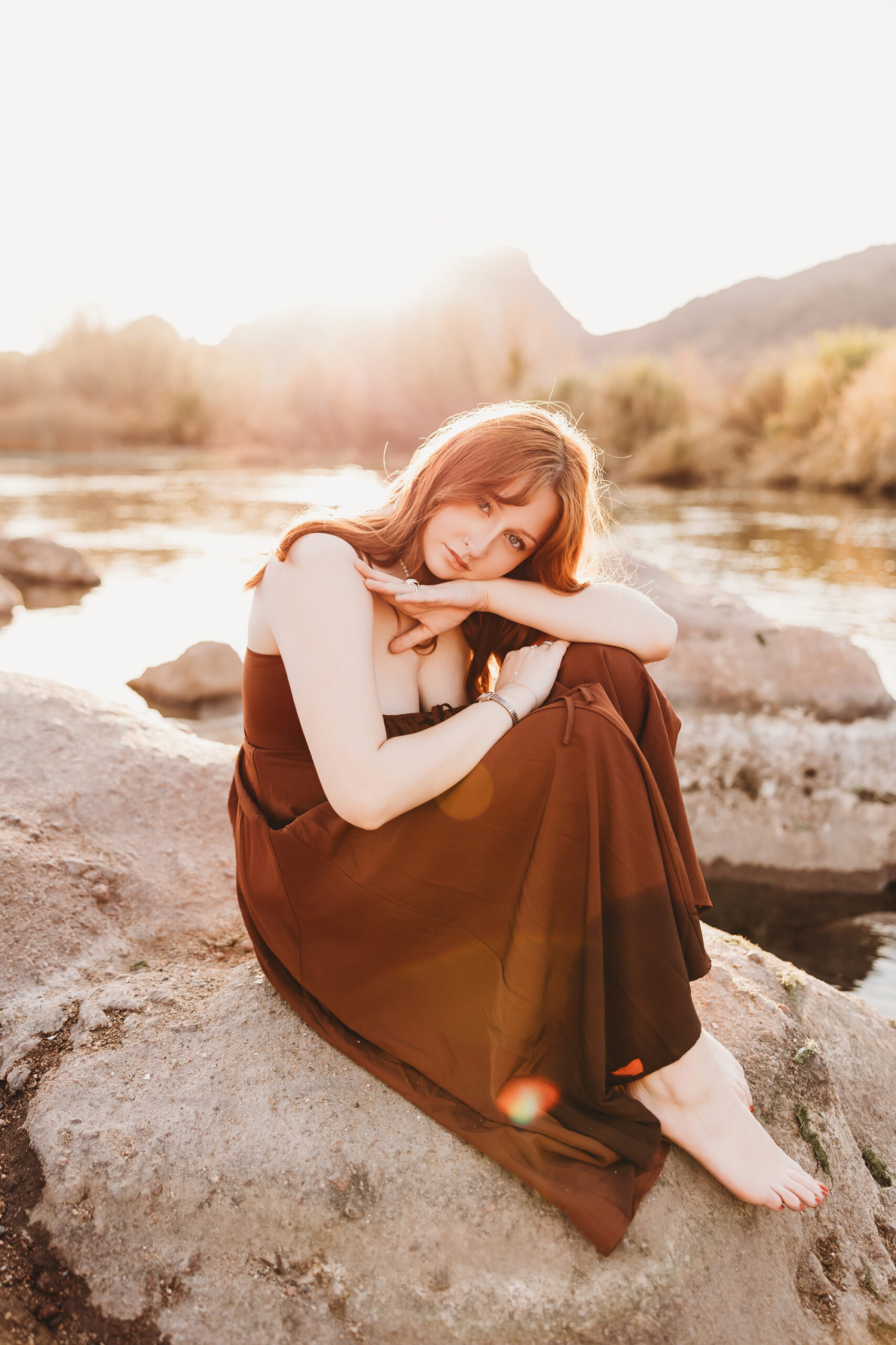 Girl in red dress posing on rock at salt river in Phoenix Arizona for senior session