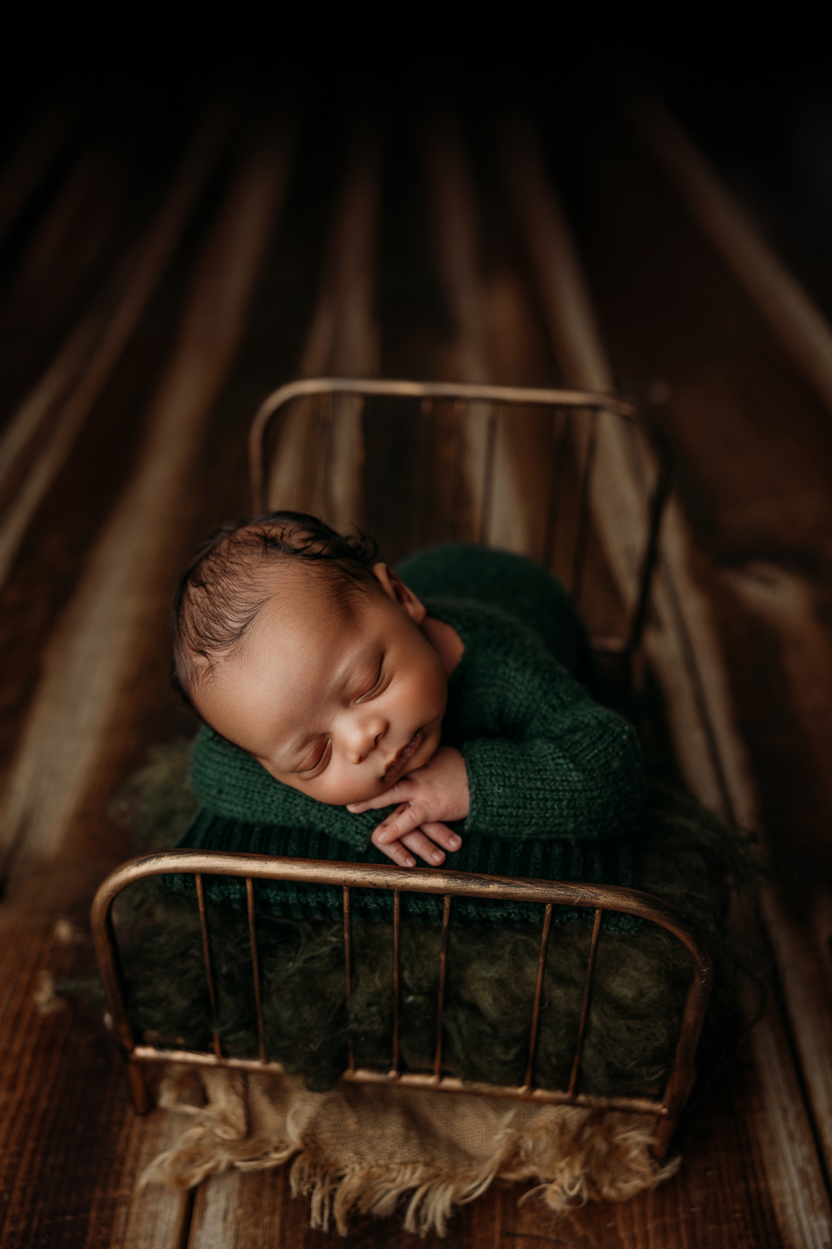 baby boy in hand knit green romper in phoenix newborn session in metal bed on wood floor