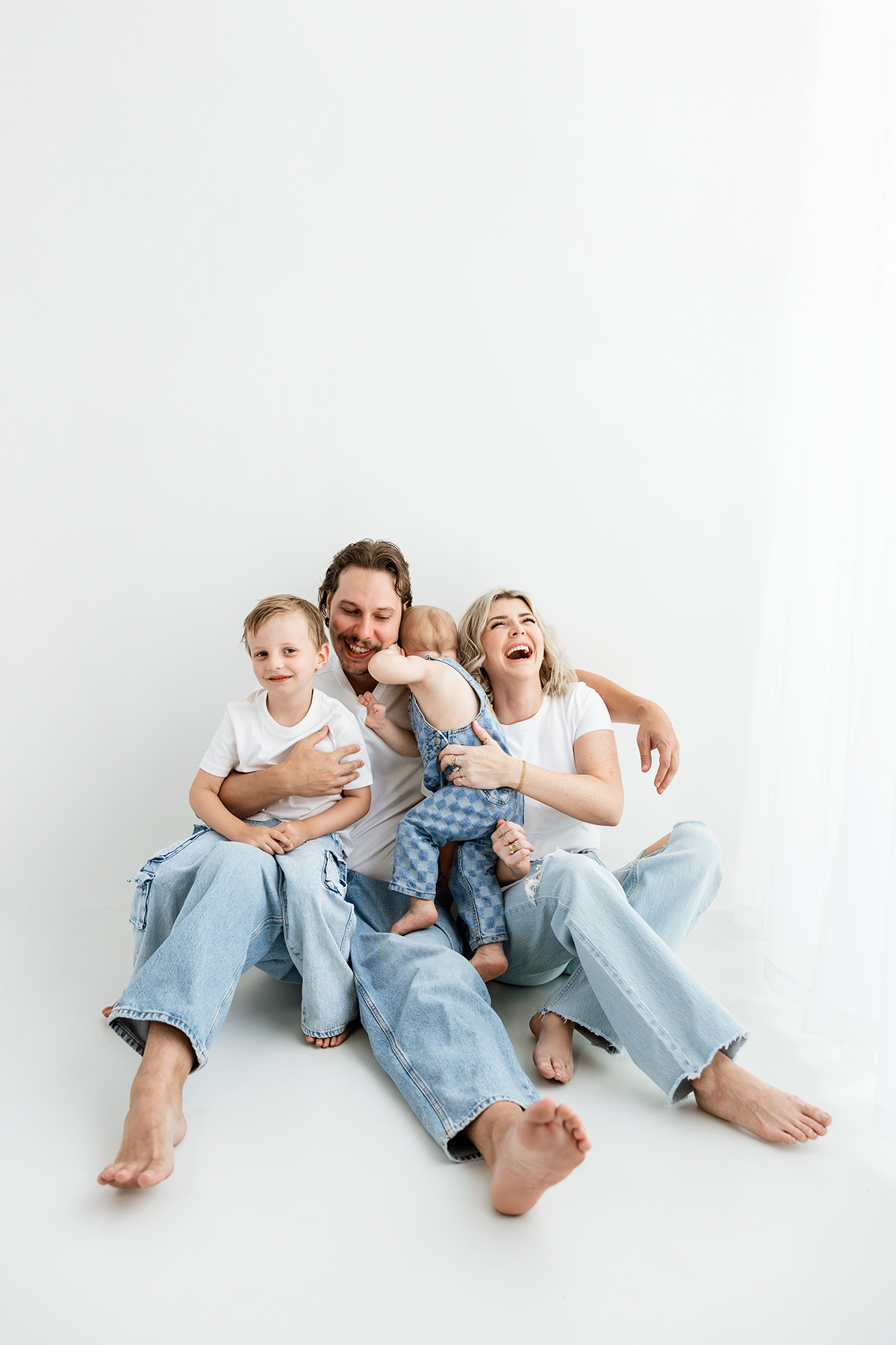 Family of 4 playing on phoenix photography studio floor in jeans and white shirt