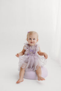 1 year old girl posing during a cake smash photoshoot in phoenix in purple outfit