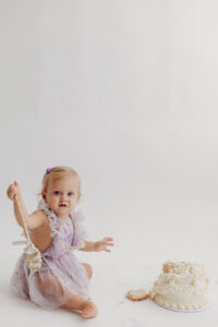 1 year old girl posing during a cake smash photoshoot in phoenix in purple outfit with cake