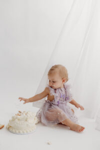1 year old girl posing during a cake smash photoshoot in phoenix in purple outfit playing with cake