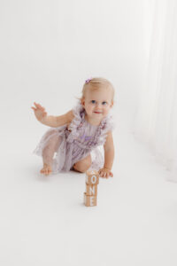 1 year old girl posing during a cake smash photoshoot in phoenix in purple outfit with wood blocks