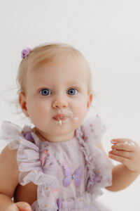 1 year old girl posing during a cake smash photoshoot in phoenix in purple outfit close up with cake on face
