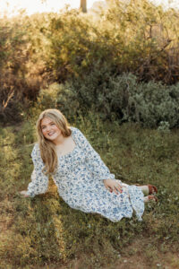 high school senior wearing white dress with blue flowers in arizona desert during phoenix senior sunset photoshoot