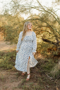 high school senior wearing white dress with blue flowers in arizona desert during phoenix senior sunset photoshoot
